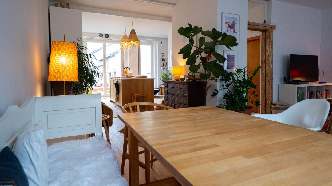 Blick in ein Wohn-Ess-Zimmer eines sanierten Hauses mit einem großen Esstisch, angrenzender Küche mit Blick auf die Terasse