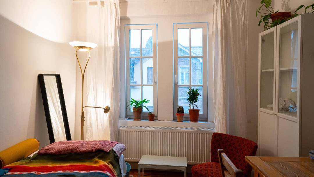 Blick in das Wohnzimmer eines sanierten Hauses mit einem Sofa mit Decken und Kissen, einem Spiegel, einem Schrank sowie Tisch und Stuhl