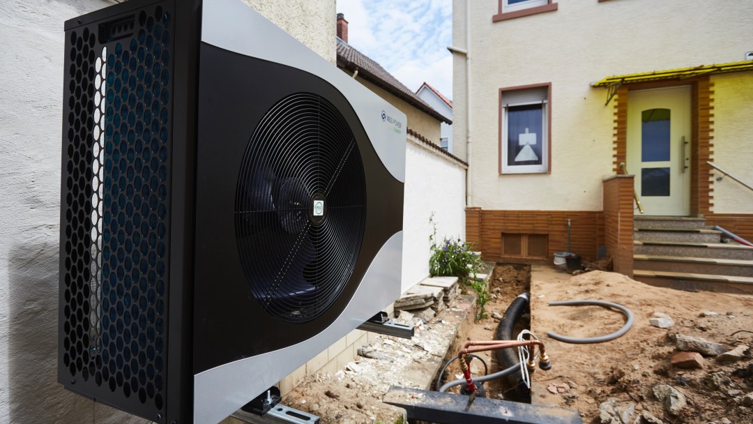 Ansicht einer Wärempumpe an einer Gartenmauer vor einem Haus in Frontansicht