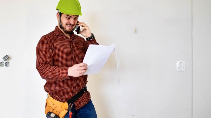 Handwerker steht in einem Zimmer eines Gebäudes, dass energieeffizient saniert wird. 