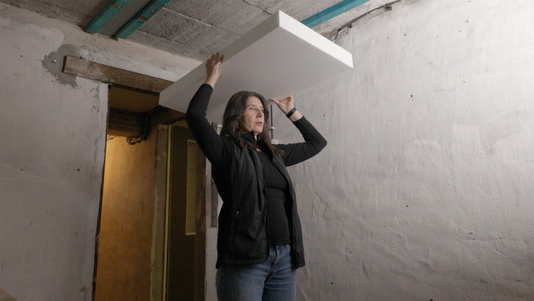 Eine Energieeffizienz-Expertin steht im Keller und trägt eine Dämmplatte
