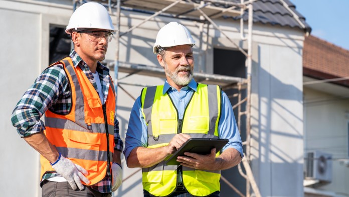 Zwei Energieeffizienz-Experten mit Sicherheitshelm und Warnwesten stehen auf der Baustelle eines Neubaus.