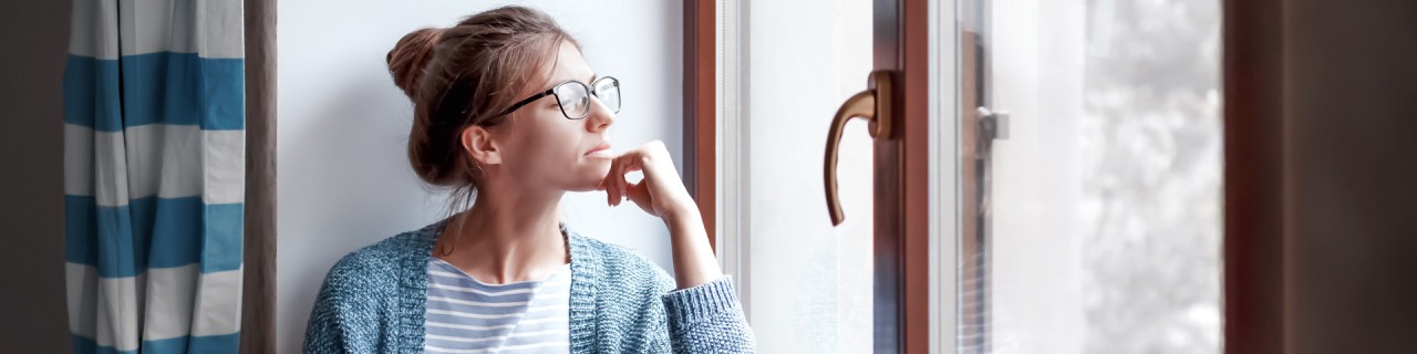 Frau sitzt auf der Fensterbank und schaut aus dem Fenster