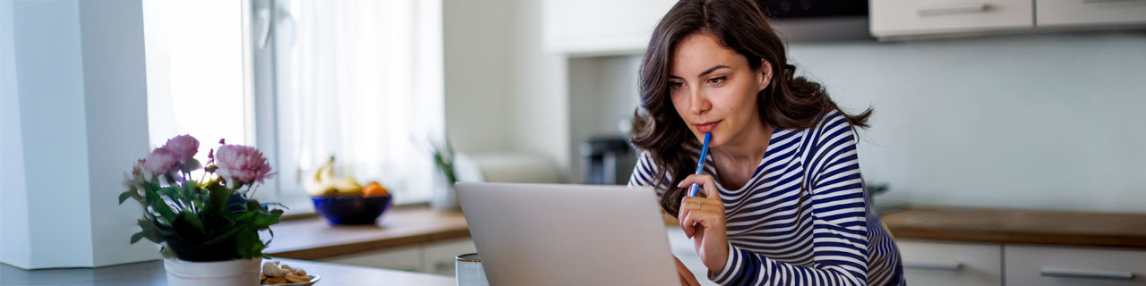 Frau steht in einer Wohnküche am Sideboard Laptop und arbeitet fokusiert