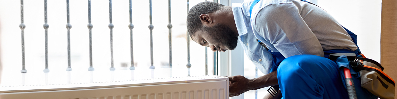 Handwerker, der eine Heizung in einem Wohnraum einbaut und mit einer Zange fixiert.