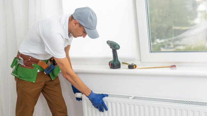 Handwerker, der eine Heizung in einem Wohnraum einbaut und mit einer Zange fixiert.