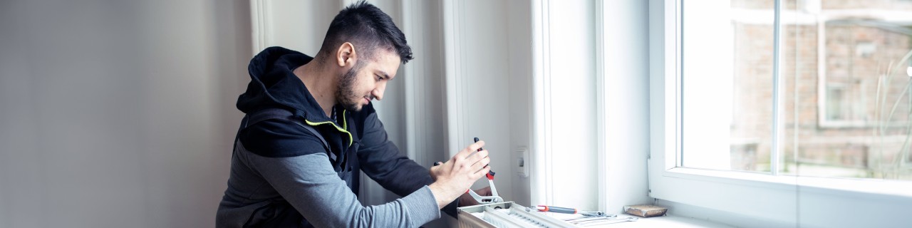 Handwerker, der eine Heizung in einem Wohnraum einbaut und mit einer Zange fixiert.