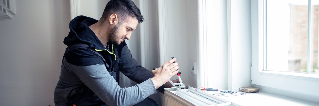 Handwerker, der eine Heizung in einem Wohnraum einbaut und mit einer Zange fixiert.