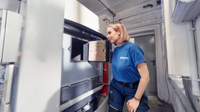 Anlagenmechanikerin öffnet Klappe einer Pelletheizung und schaut hinein.