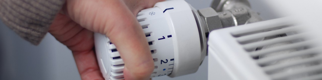 Eine Hand dreht am Temperaturregler des Heizkörpers.