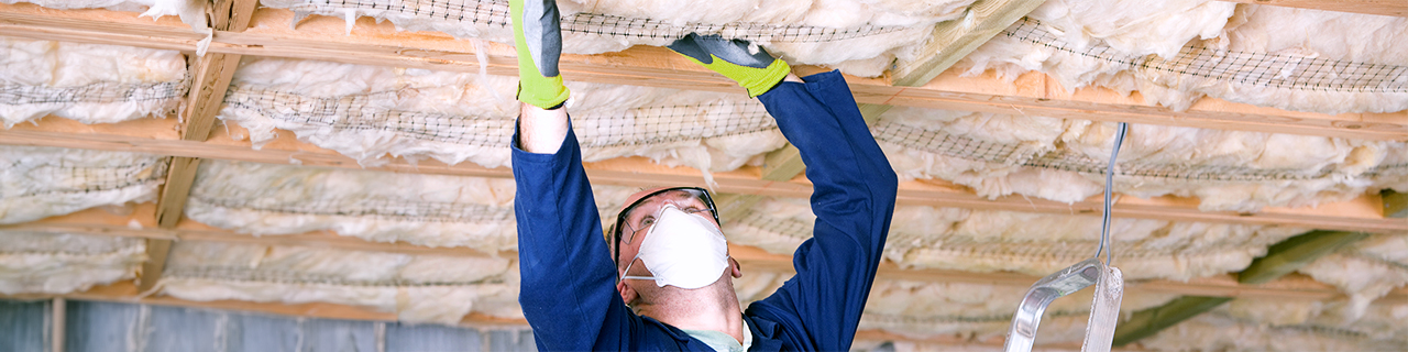 Ein Handwerker in Schutzkleidung dämmt eine Kellerdecke