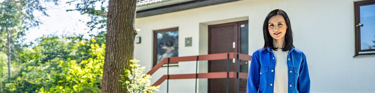 Junge Frau steht selbstbewusst vor einem Haus
