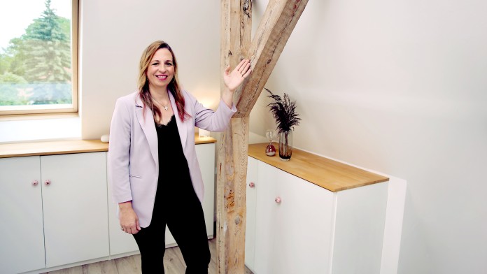 Eine Frau steht in einem Haus und zeigt einen Fachwerkbalken