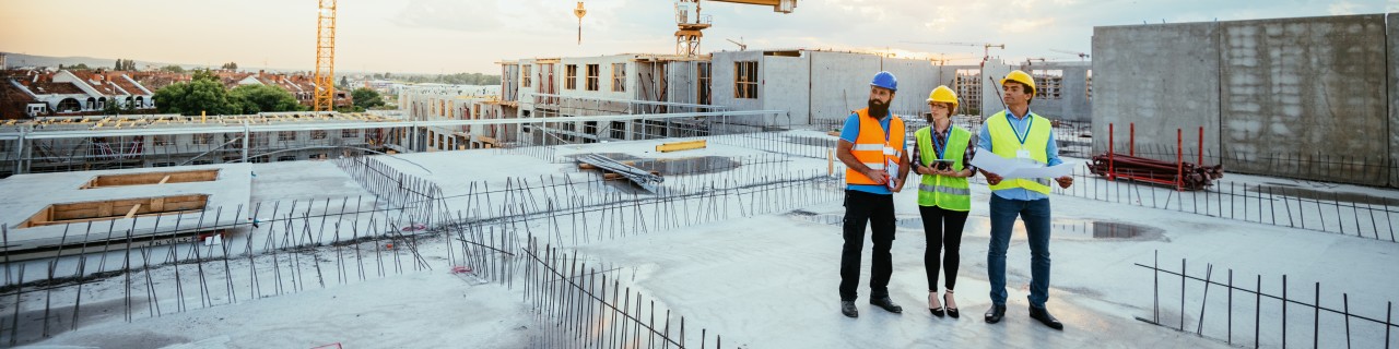 Personen mit Warmweste stehen auf dem Dach eines sich im Bau befindlichen Mehrfamilienhauses