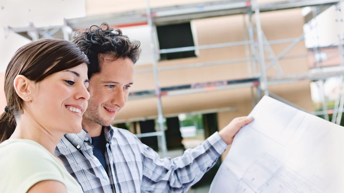 Ein Paar steht mit Bauplan vor seinem neuen Haus.