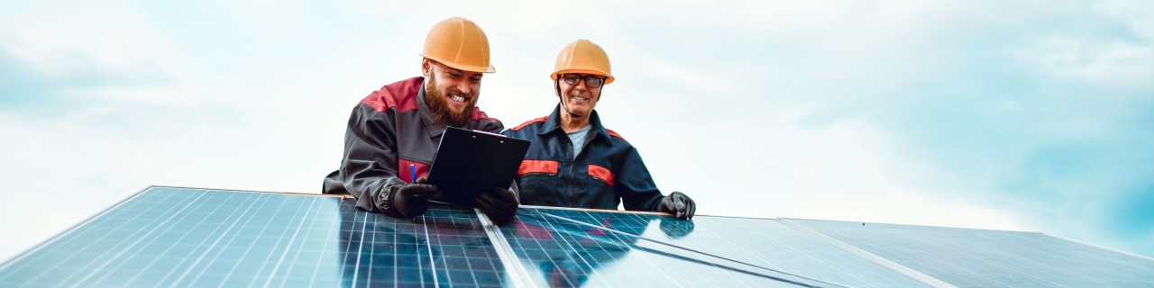 Zwei Handwerker installieren Solarpanele für eine Photovoltaik-Anlage auf dem Dach.