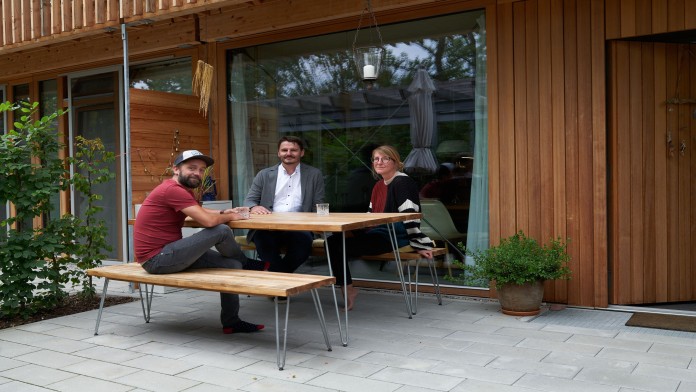 Drei Personen sitzen zusammen an einem Tisch im Freien