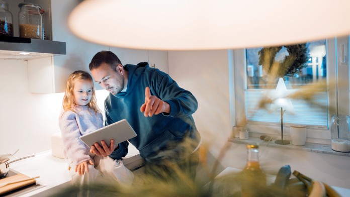 Vater und Tochter steuern die Beleuchtung ihres Smart Homes über ein Tablet.