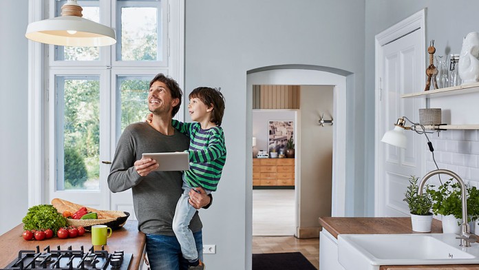 Vater mit Kind auf dem Arm, schauen beide begeistert die Lampe an, welche über das Tablett gesteuert wird.