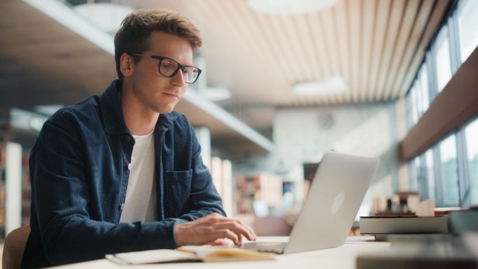Student arbeitet konzentriert am Laptop in einer Bibliothek.