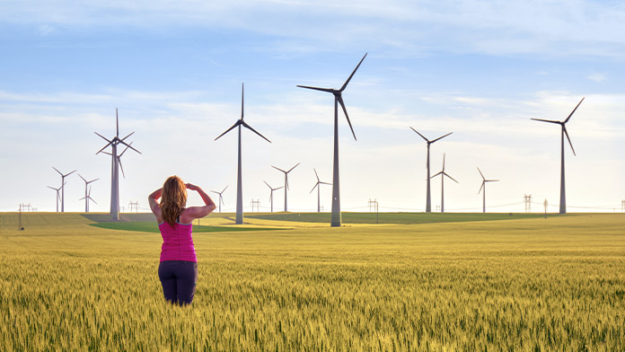 Woman from behind standing in corn field, in background many wind turbines