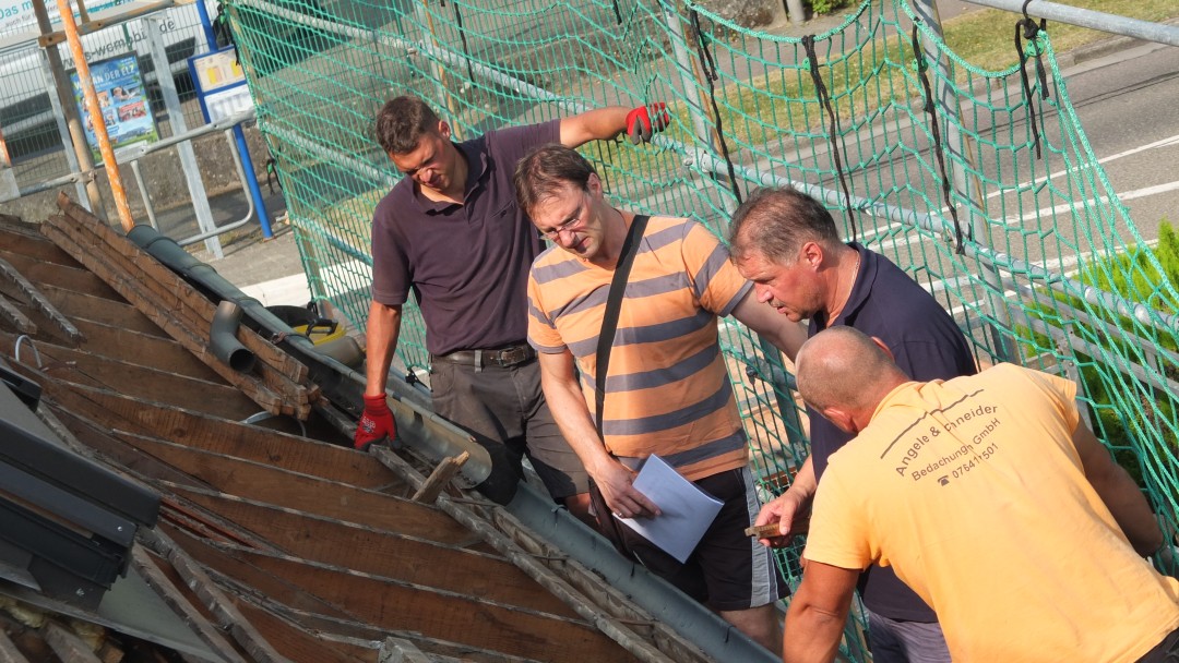 Energieberater und Handwerker begutachten das Dach eines sanierungsbedüftigen Hauses