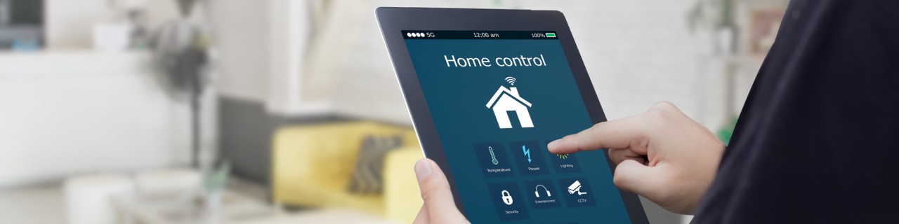 Hände halten Tablet mit Smart Home App, unscharf im Hintergrund ein Wohnzimmer