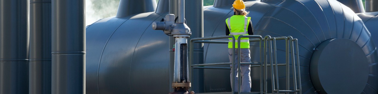 Technikerin steht auf einer Arbeitsbühne vor einer Geothermie-Anlage