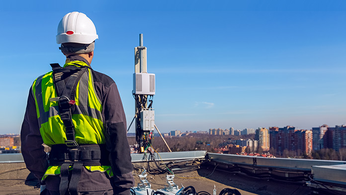 Industrial climber with helmet on skyscraper roof in front of radio mast