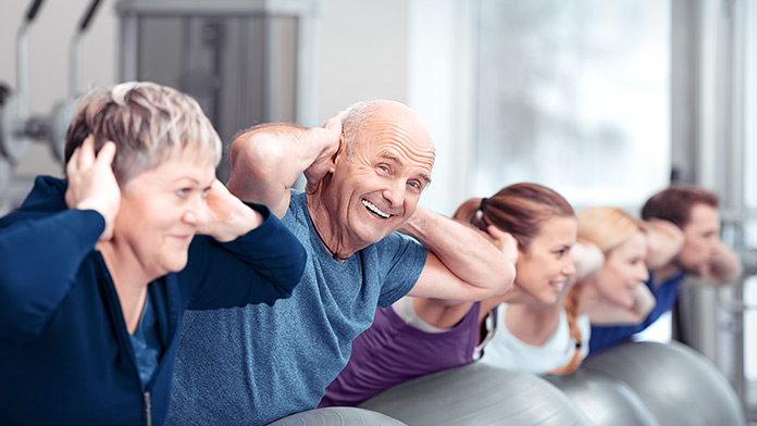 In einer Reihe machen junge und ältere Menschen Sportübungen auf Gymnastikbällen