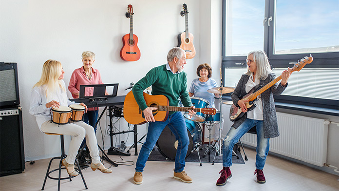 Group of 5 mature bandmembers play various instruments while indoors