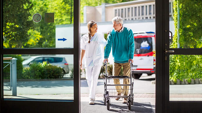 Nurse assists elderly patient with use of rollator
