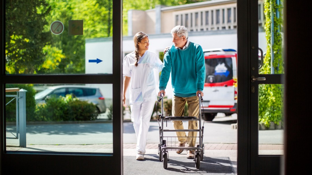 Krankenschwester unterstützt älteren Patienten bei der Benutzung eines Gehwagens