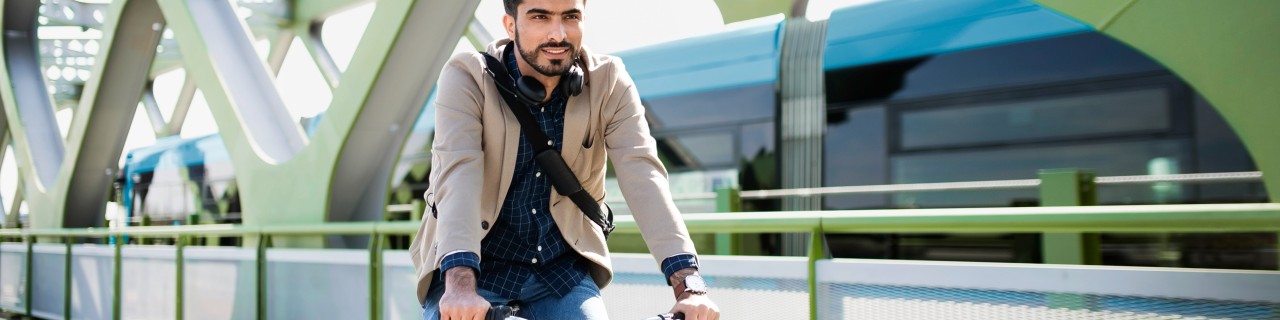 Junger Geschäftsmann fährt mit dem Fahrrad über eine Brücke zur Arbeit