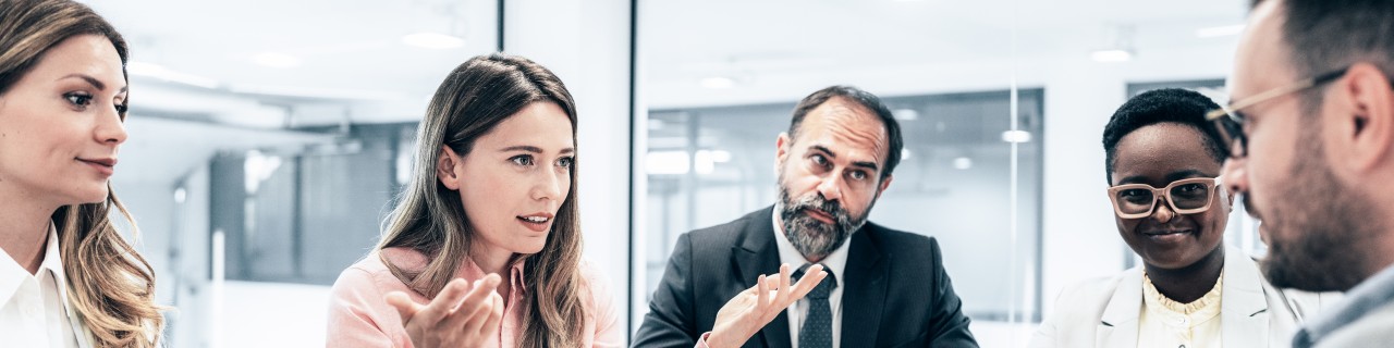 Porträt einer Finanzberaterin, die im Büro vor einem Computer sitzt und einen jungen Mann berät