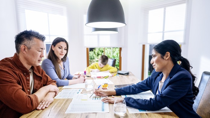 Eine Finanzberaterin präsentiert einer Familie am Tisch eine Tabelle.