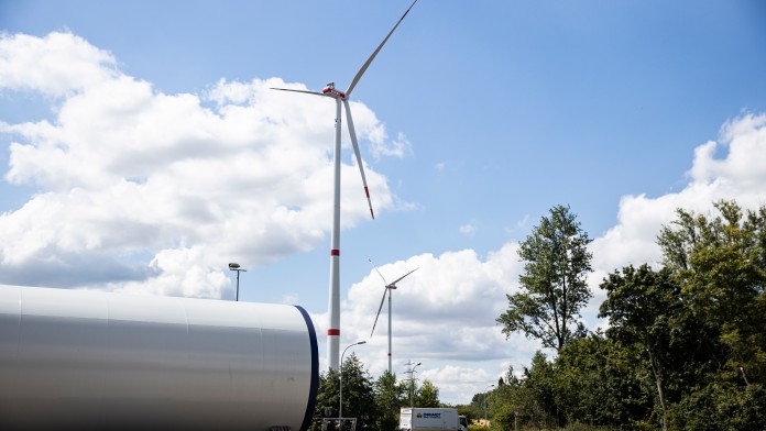 Ein großer Tank dahinter zwei Windräder und ein LKW, links Wald