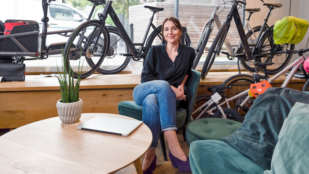 Eine Frau sitzt in einem Laden, im Hintergrund stehen Fahrräder im Schaufenster