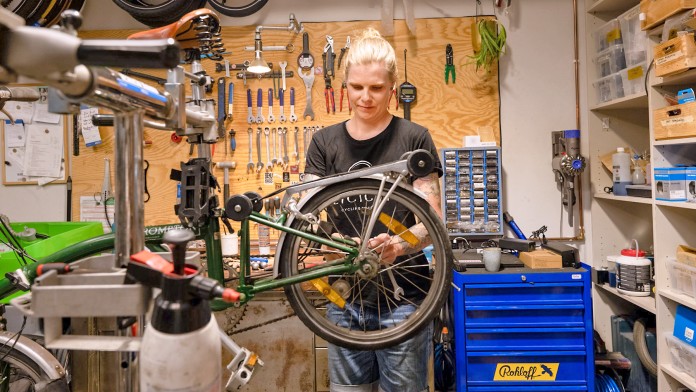 Eine Frau steht in einer Werkstatt und repariert ein Fahrrad