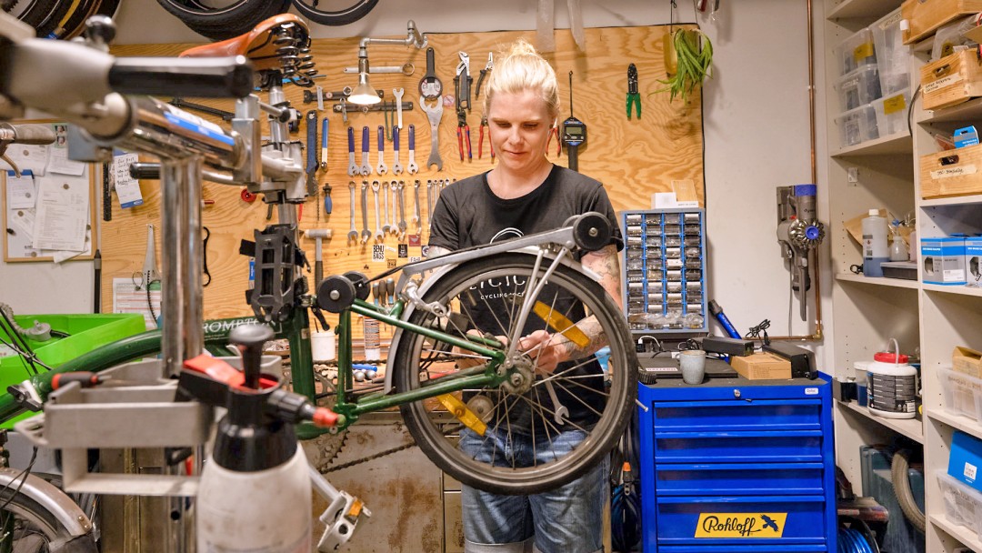 Eine Frau steht in einer Werkstatt und repariert ein Fahrrad