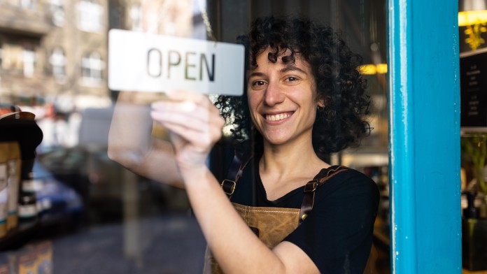 Eine lächelnde Frau mit Open-Schild an einer Ladentür