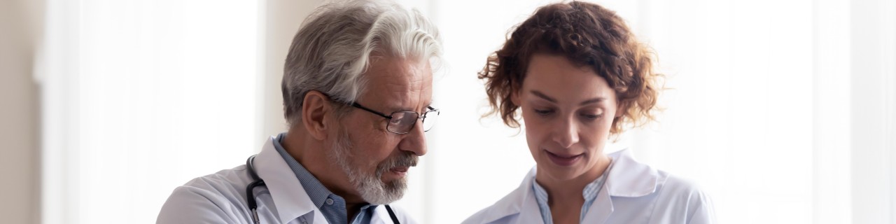 Ein älterer Arzt und eine junge Ärztin schauen gemeinsam auf ein Tablet