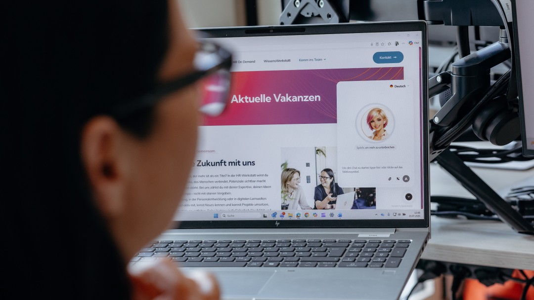 Anwenderin sitzt vor dem aufgeklappten Laptop und arbeitet gemeinsam mit dem KI-Voice-Agenten Nora