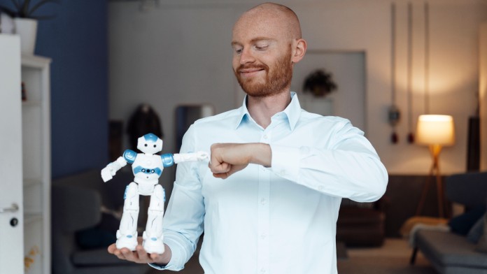 Mann hält einen kleinen Roboter auf seiner Hand und ist mit diesem Faust an Faust