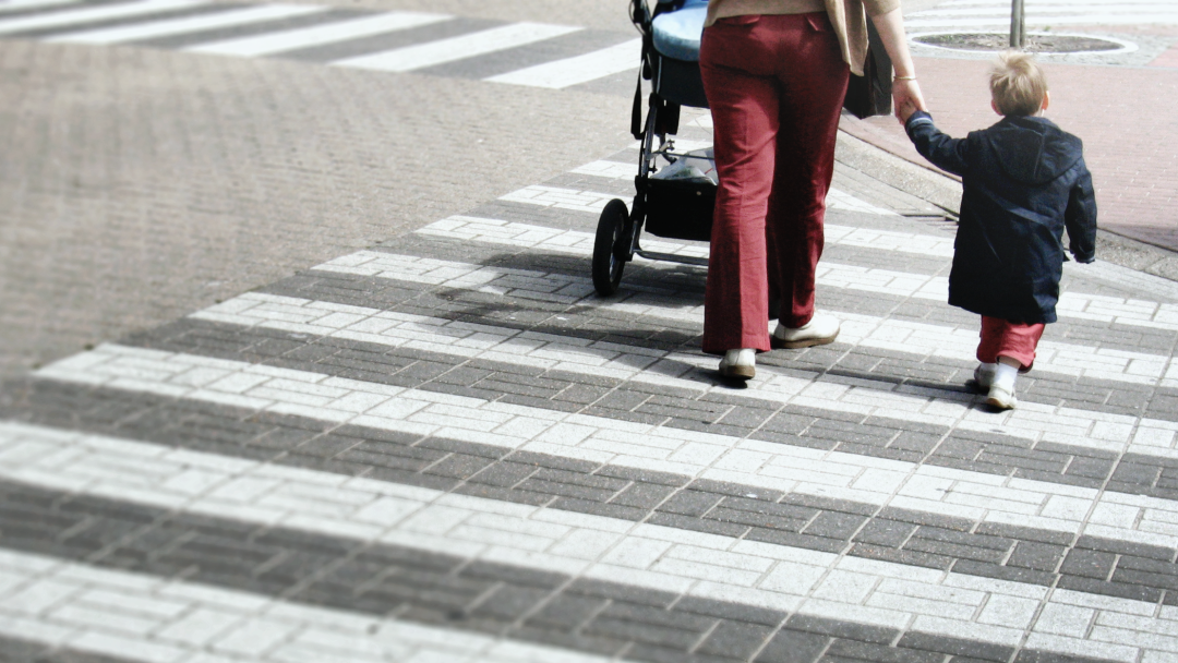 Eine Frau mit Kinderwagen und einem kleinen Kind überquert einen Zebrastreifen