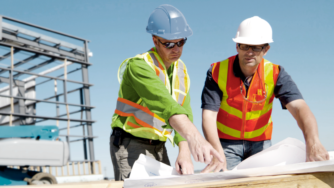 Zwei Architekten auf einer Baustelle blicken auf eine Bauzeichnung
