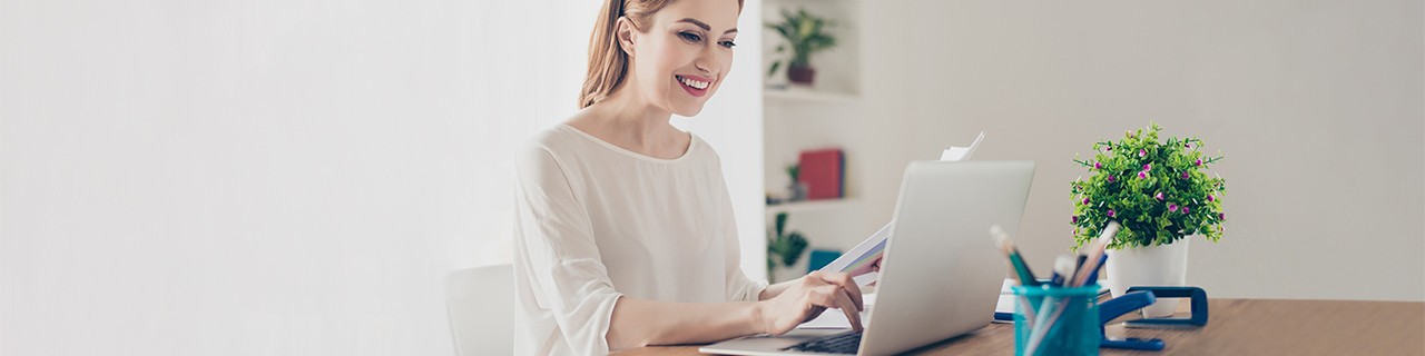 Eine Frau sitzt fröhlich am Laptop und hält Dokumente in der Hand