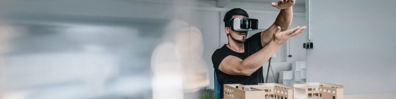 Junger Mann mit Virtual Reality Brille steht vor einem Architekturmodell