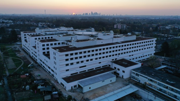 Ansicht auf den Klinikersatzneubau in der Dämmerung, im Hintergrund Frankfurter Skyline