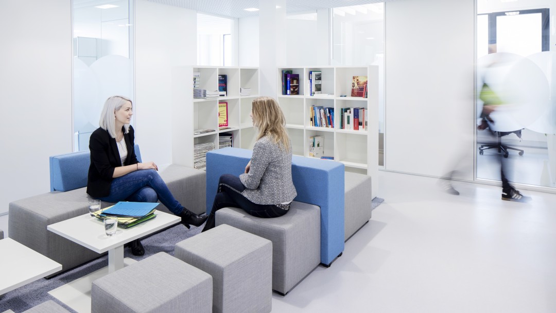 2 sitzende Frauen im Gespräch in einer modernen Sitzecke im Verwaltungsgebäude